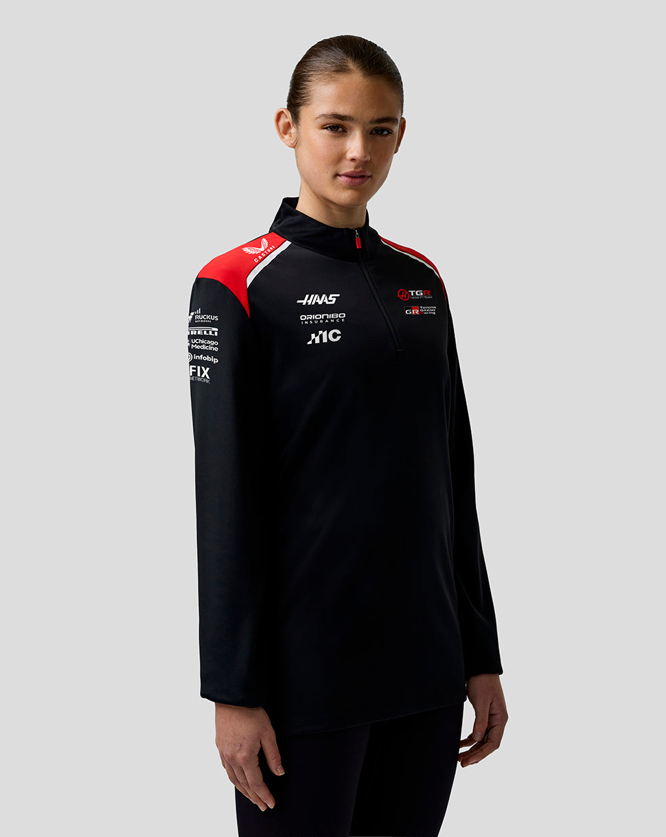Person wearing a black sports jacket with red and white accents on a gray background