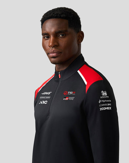 Person wearing a black sports jacket with red and white accents on a gray background