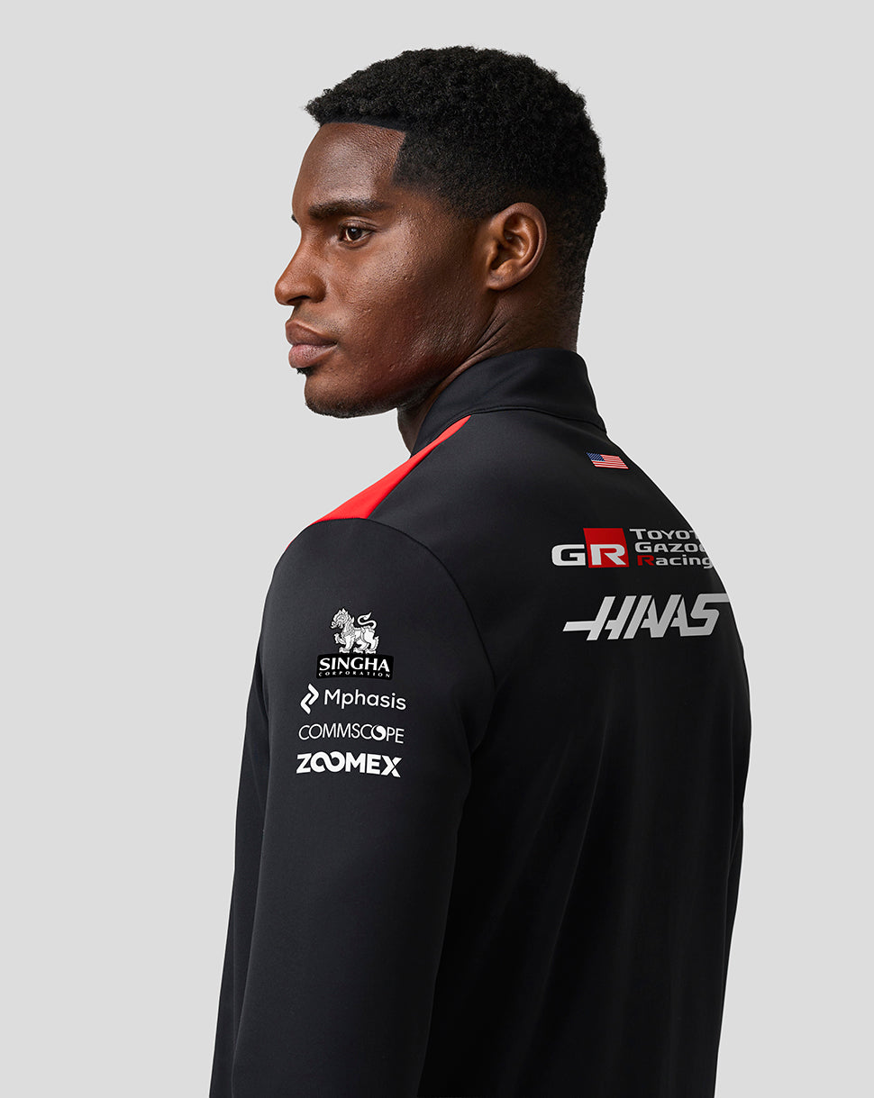 Person wearing a black racing jacket with various sponsor logos on a gray background