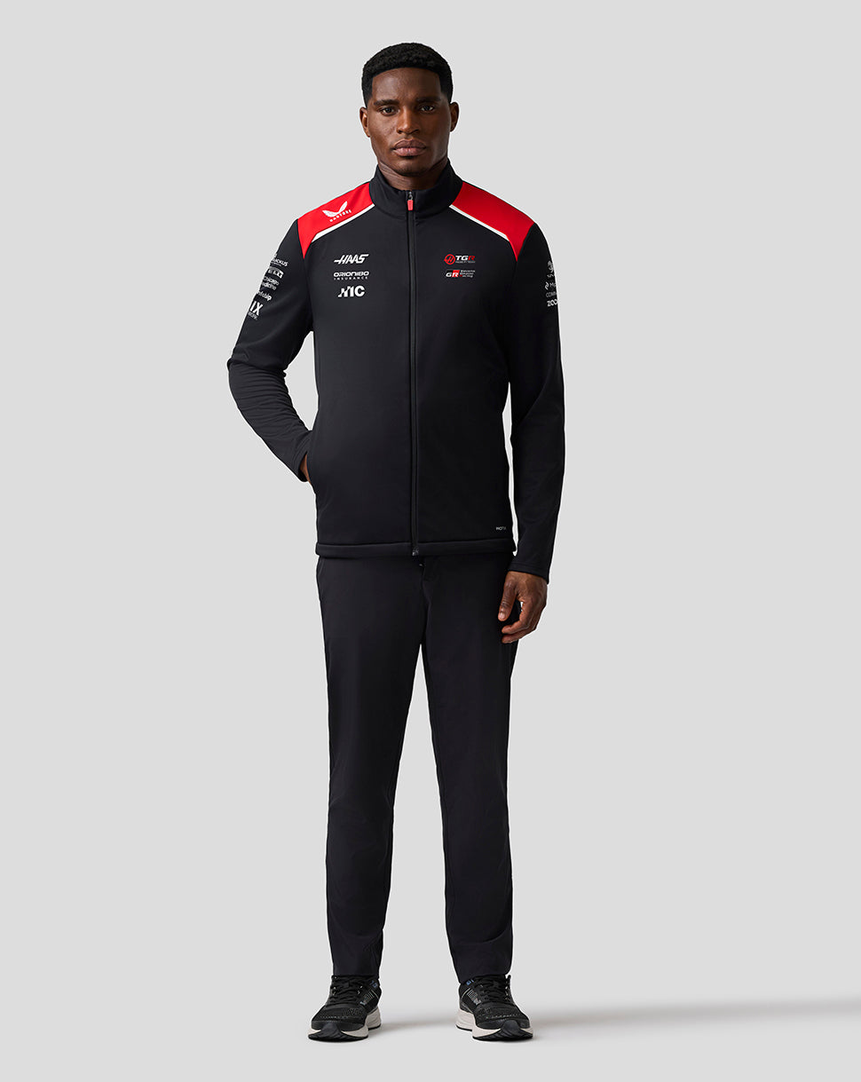 Person wearing a black tracksuit with red accents on a gray background
