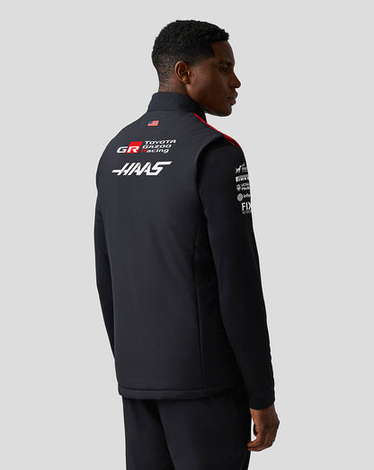 Person wearing a black jacket with sponsor logos on a gray background