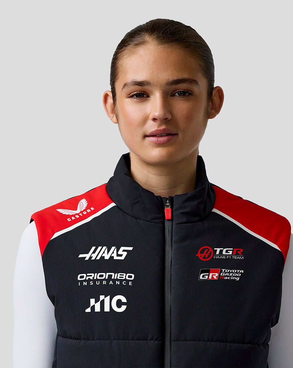 Person wearing a black racing jacket with various logos on a gray background