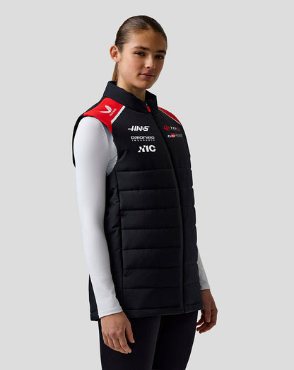 Person wearing a black quilted vest with sponsor logos on a gray background