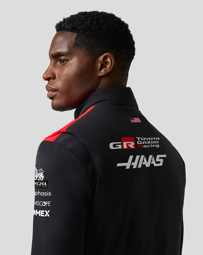 Person wearing a black racing suit with various sponsor logos on a gray background