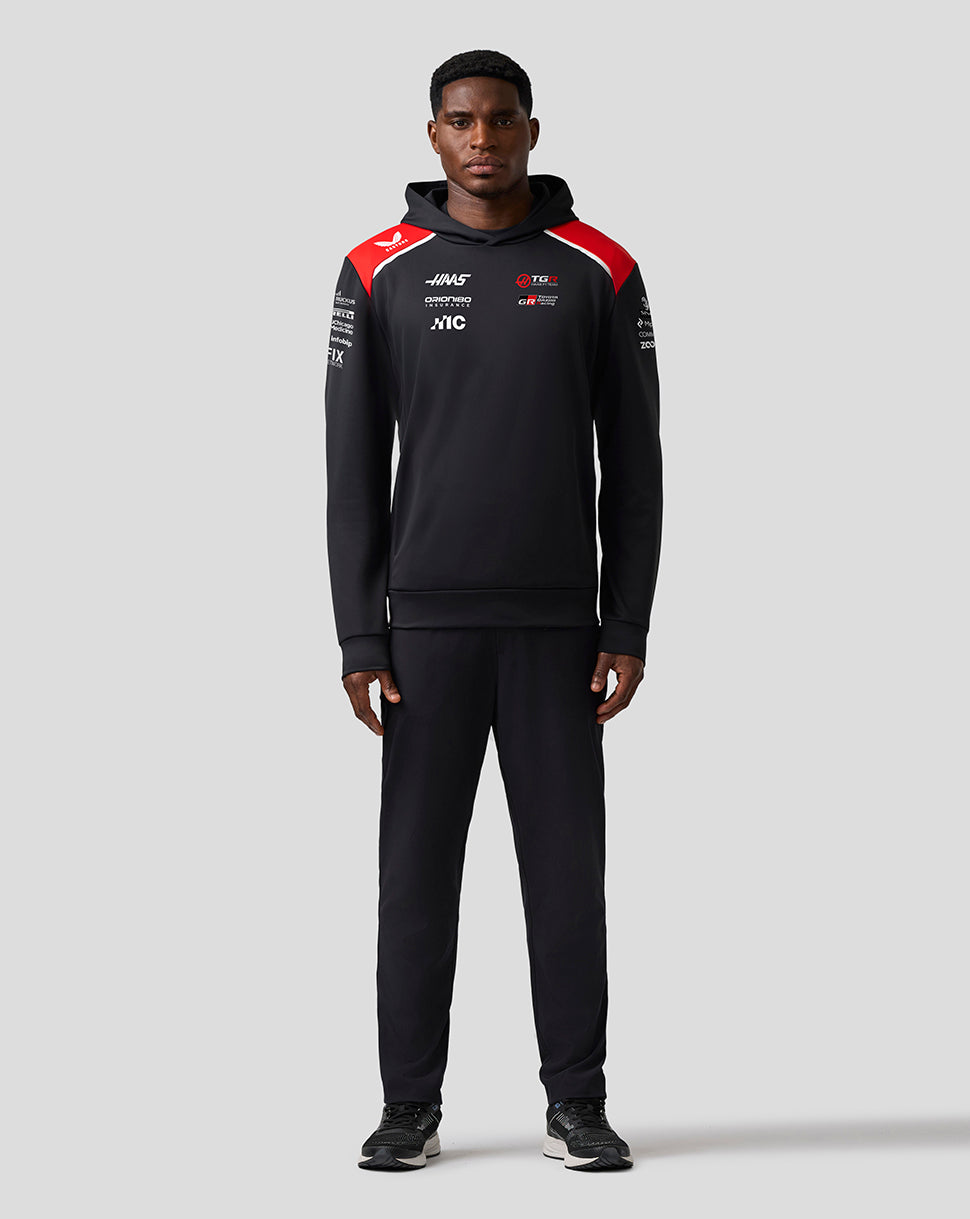 Person wearing a black tracksuit with red and white accents on a gray background
