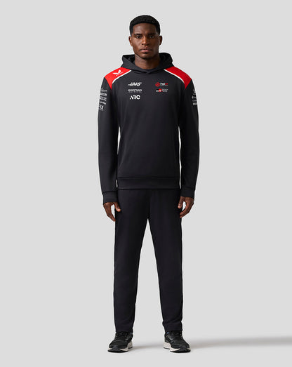 Person wearing a black tracksuit with red and white accents on a gray background
