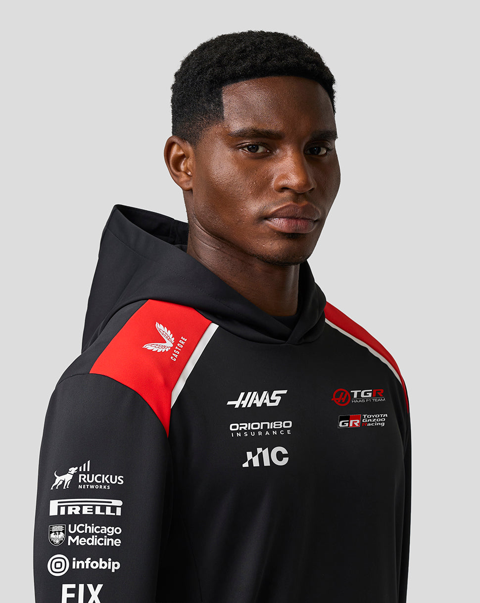 Person wearing a black hoodie with various logos on a gray background