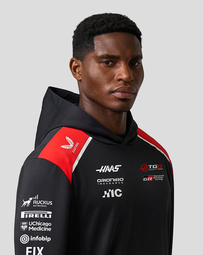 Person wearing a black hoodie with various logos on a gray background