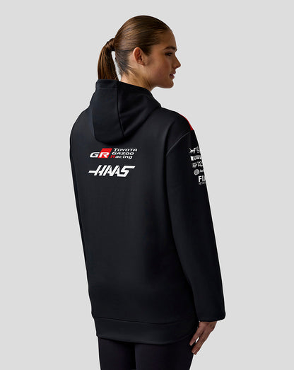 Person wearing a black hoodie with racing team logos on a gray background