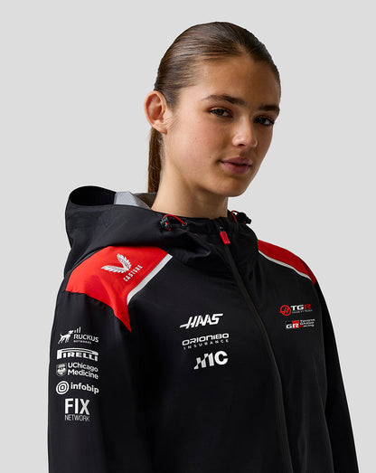 Person wearing a black hoodie with various logos on a gray background