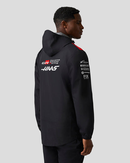 Person wearing a black jacket with sponsor logos on the back against a white background