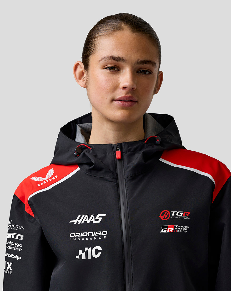 Person wearing a black and red jacket with various logos on a gray background