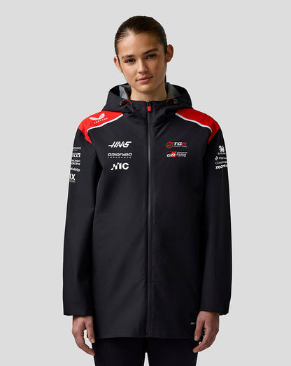 Person wearing a black jacket with sponsor logos on a gray background