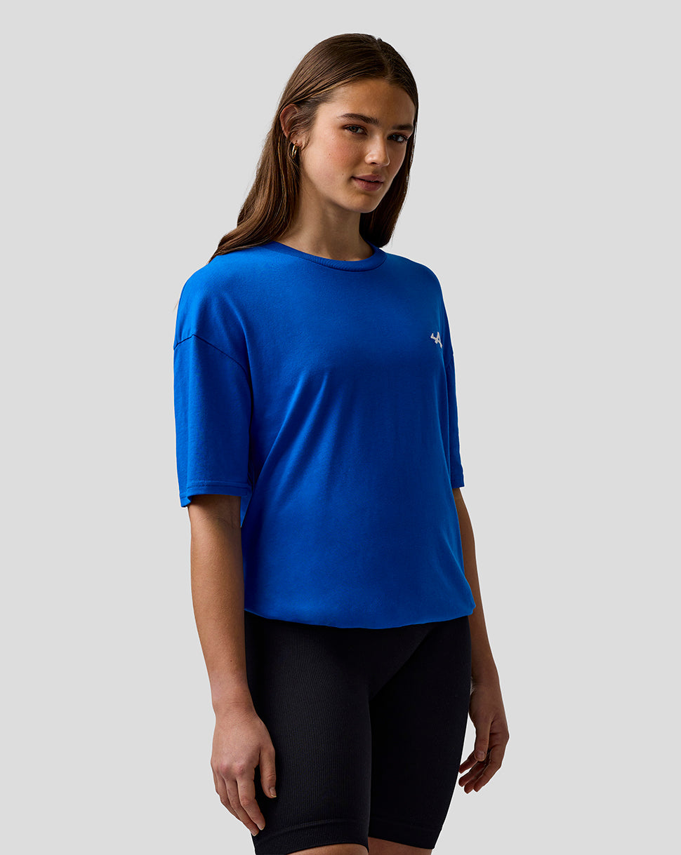 Portrait of a woman wearing a lapis blue relaxed fit T-shirt with a small left chest logo.
