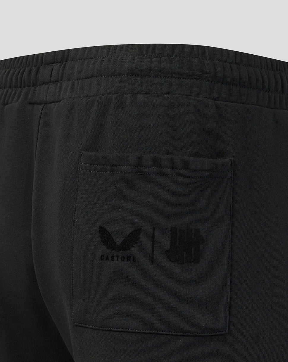 Black joggers with a brand logo on the pocket against a light gray background