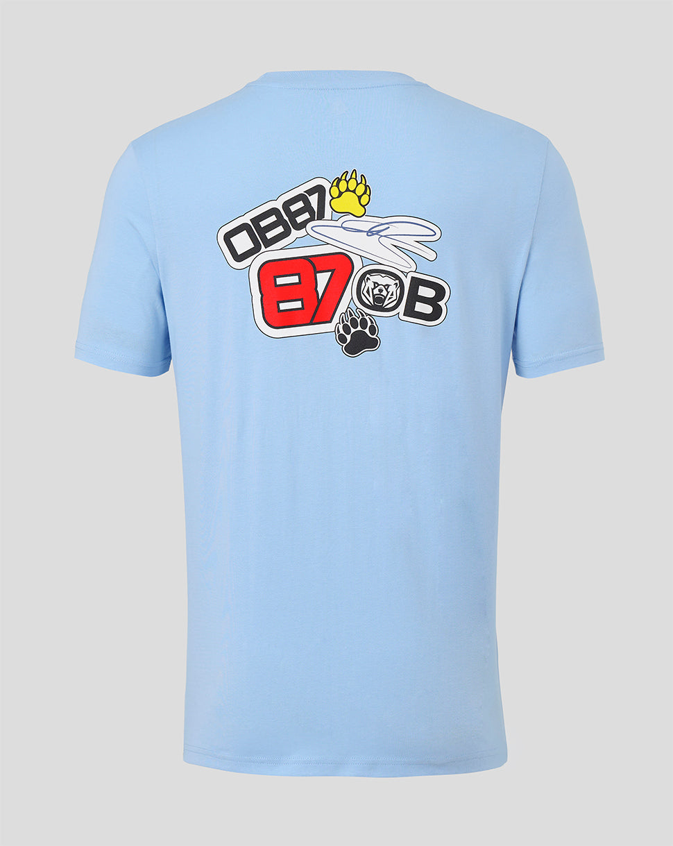 A light blue short-sleeve t-shirt shown from the back, featuring a large graphic print on the upper back with the text 'OBB 87 OBB' in red, white, and black, along with a yellow paw print and a small black bear graphic, set against a solid light gray background.