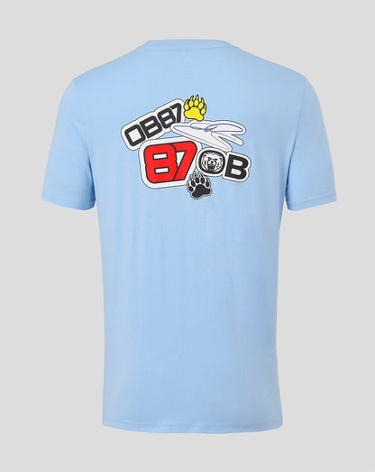 A light blue short-sleeve t-shirt shown from the back, featuring a large graphic print on the upper back with the text 'OBB 87 OBB' in red, white, and black, along with a yellow paw print and a small black bear graphic, set against a solid light gray background.