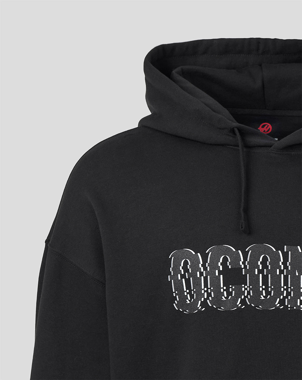 Close-up of a black pullover hoodie with a large white and black glitch-style 'OCOM' graphic across the chest, shown against a light gray background.