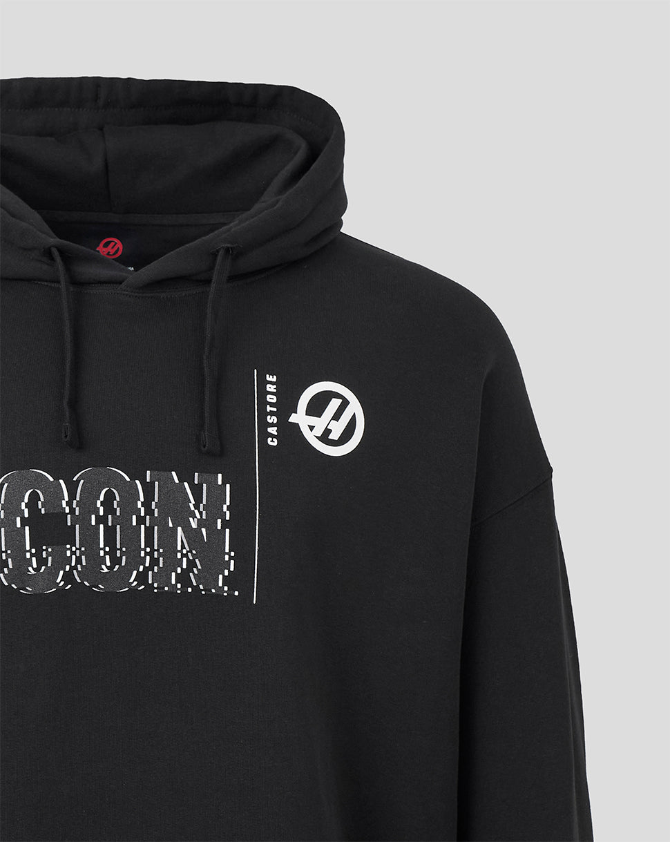 Close-up of a black pullover hoodie with white printed graphics, including a circular logo on the chest and partial large text on the front, shown against a light gray background.