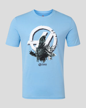 A light blue short-sleeve crewneck t-shirt featuring a large graphic print of Godzilla emerging from a circular emblem, with the logo printed below the graphic, shown against a solid gray background.